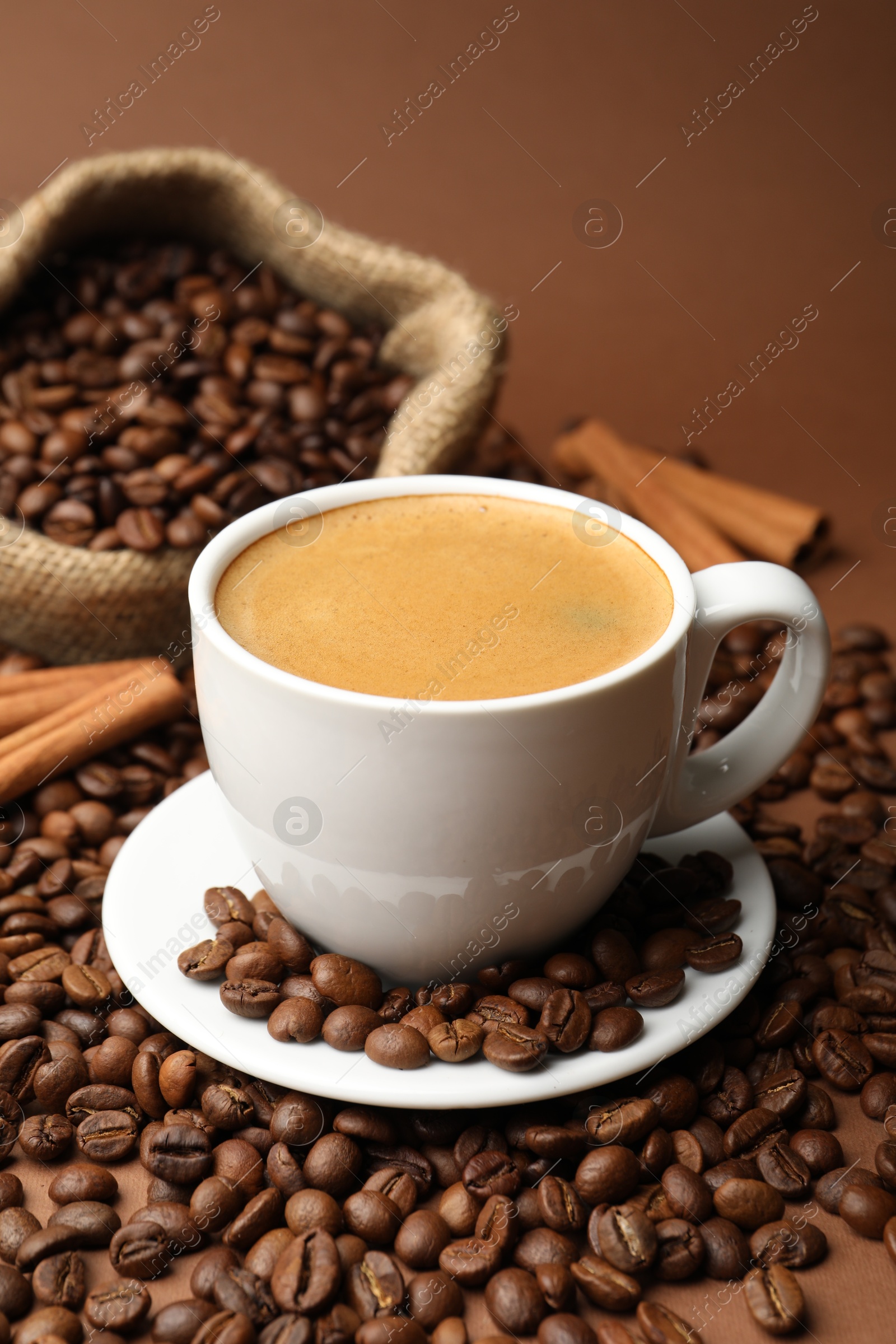 Cup of hot coffee, beans and cinnamon on brown background, closeup Photo of Cup of hot coffee, beans and cinnamon on brown background, closeup