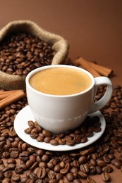 Photo of Cup of hot coffee, beans and cinnamon on brown background, closeup
