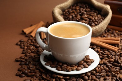 Photo of Cup of hot coffee, beans and cinnamon on brown background, closeup