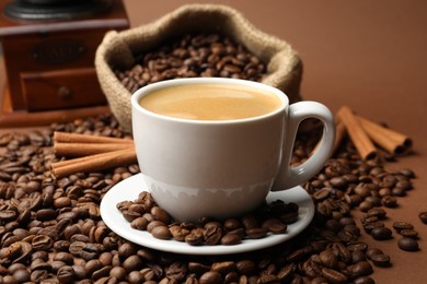 Photo of Cup of hot coffee, beans and cinnamon on brown background, closeup