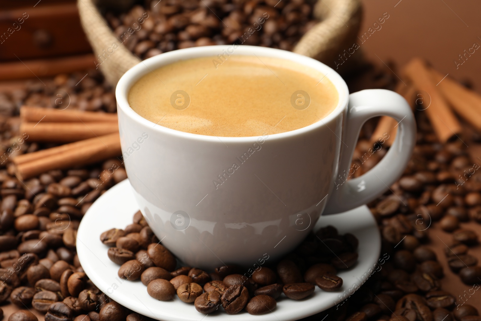 Cup of hot coffee, beans and cinnamon on brown background, closeup Photo of Cup of hot coffee, beans and cinnamon on brown background, closeup