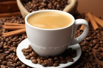 Photo of Cup of hot coffee, beans and cinnamon on brown background, closeup