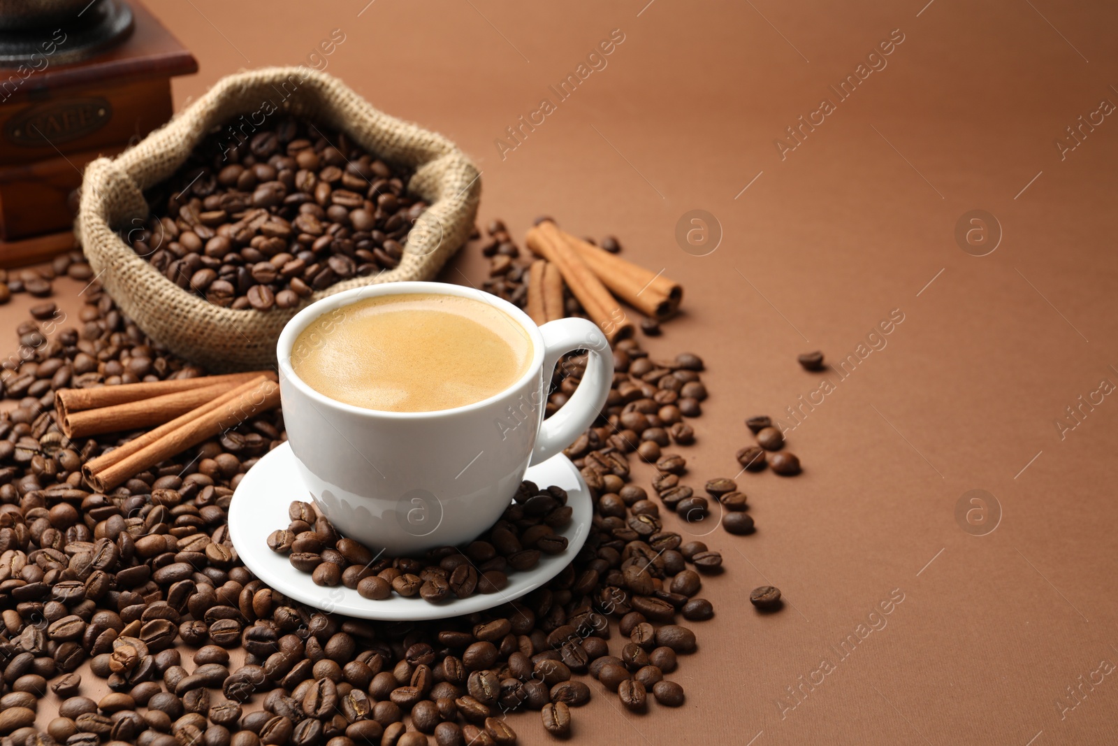 Cup of hot coffee, beans and cinnamon on brown background, space for text Photo of Cup of hot coffee, beans and cinnamon on brown background, space for text