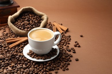 Photo of Cup of hot coffee, beans and cinnamon on brown background, space for text