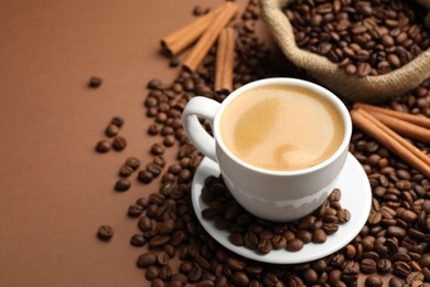 Photo of Cup of hot coffee, beans and cinnamon on brown background, closeup. Space for text