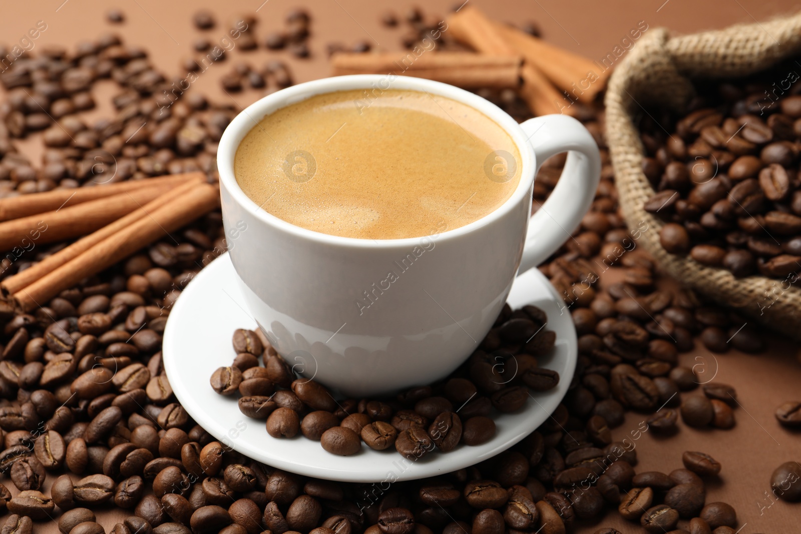 Cup of hot coffee, beans and cinnamon on brown background, closeup Photo of Cup of hot coffee, beans and cinnamon on brown background, closeup