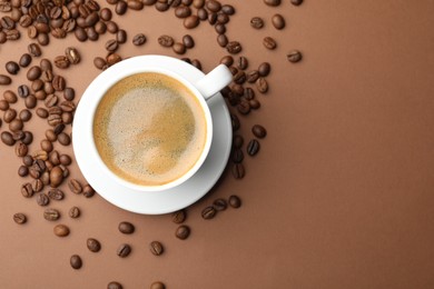 Photo of Cup of hot coffee and beans on brown background, flat lay. Space for text
