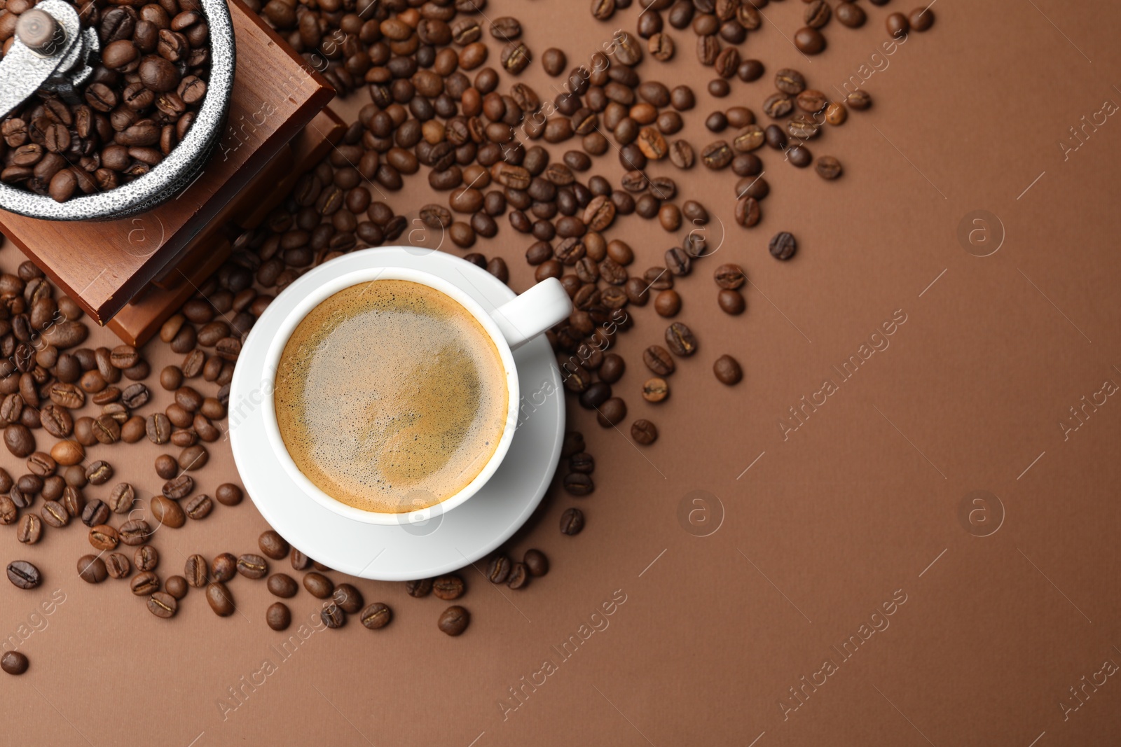 Photo of Cup of hot coffee, grinder and beans on brown background, flat lay. Space for text