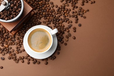 Photo of Cup of hot coffee, grinder and beans on brown background, flat lay. Space for text