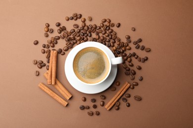Photo of Cup of hot coffee, cinnamon and beans on brown background, flat lay