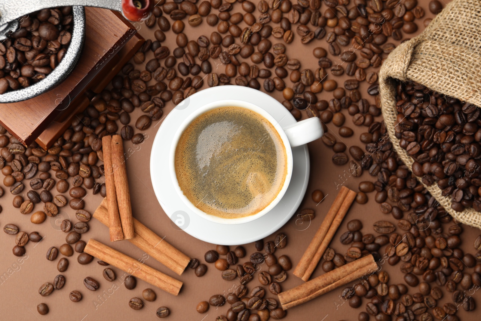 Photo of Cup of hot coffee, grinder, cinnamon and beans on brown background, flat lay