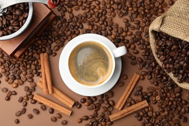 Photo of Cup of hot coffee, grinder, cinnamon and beans on brown background, flat lay