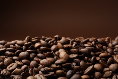 Photo of Pile of roasted coffee beans on brown background, closeup