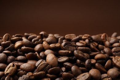 Photo of Pile of roasted coffee beans on brown background, closeup