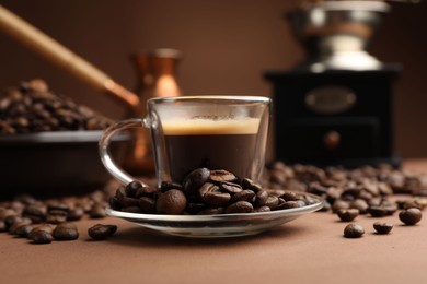 Photo of Cup of hot coffee, cezve, grinder and beans on brown background, closeup