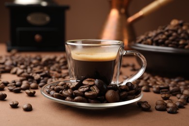 Photo of Cup of hot coffee, cezve, grinder and beans on brown background, closeup