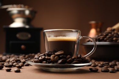Photo of Cup of hot coffee, grinder and beans on brown background, closeup