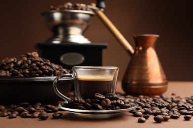 Photo of Cup of hot coffee, cezve, grinder and beans on brown background, closeup