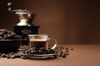 Photo of Cup of hot coffee, grinder and beans on brown background, closeup. Space for text