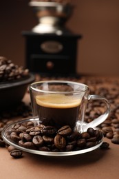 Photo of Cup of hot coffee, grinder and beans on brown background, closeup