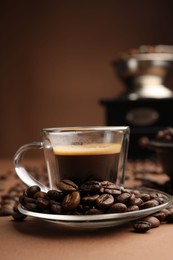 Photo of Cup of hot coffee, grinder and beans on brown background, closeup