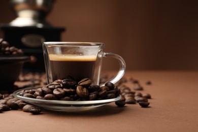 Photo of Cup of hot coffee, grinder and beans on brown background, closeup. Space for text