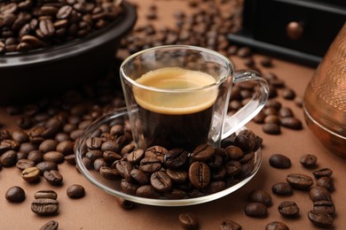 Photo of Cup of hot coffee and beans on brown background, closeup