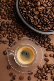 Photo of Cup of hot coffee and beans on brown background, flat lay