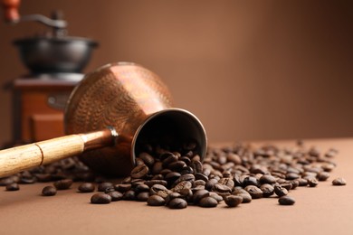 Photo of Cezve and roasted coffee beans on brown background, closeup. Space for text