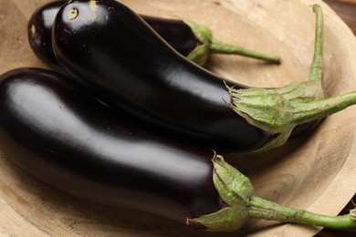 Photo of Whole fresh eggplants in wooden bowl, closeup