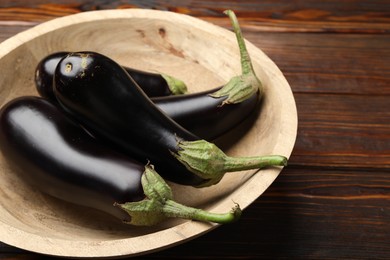Photo of Fresh eggplants in bowl on wooden table, closeup