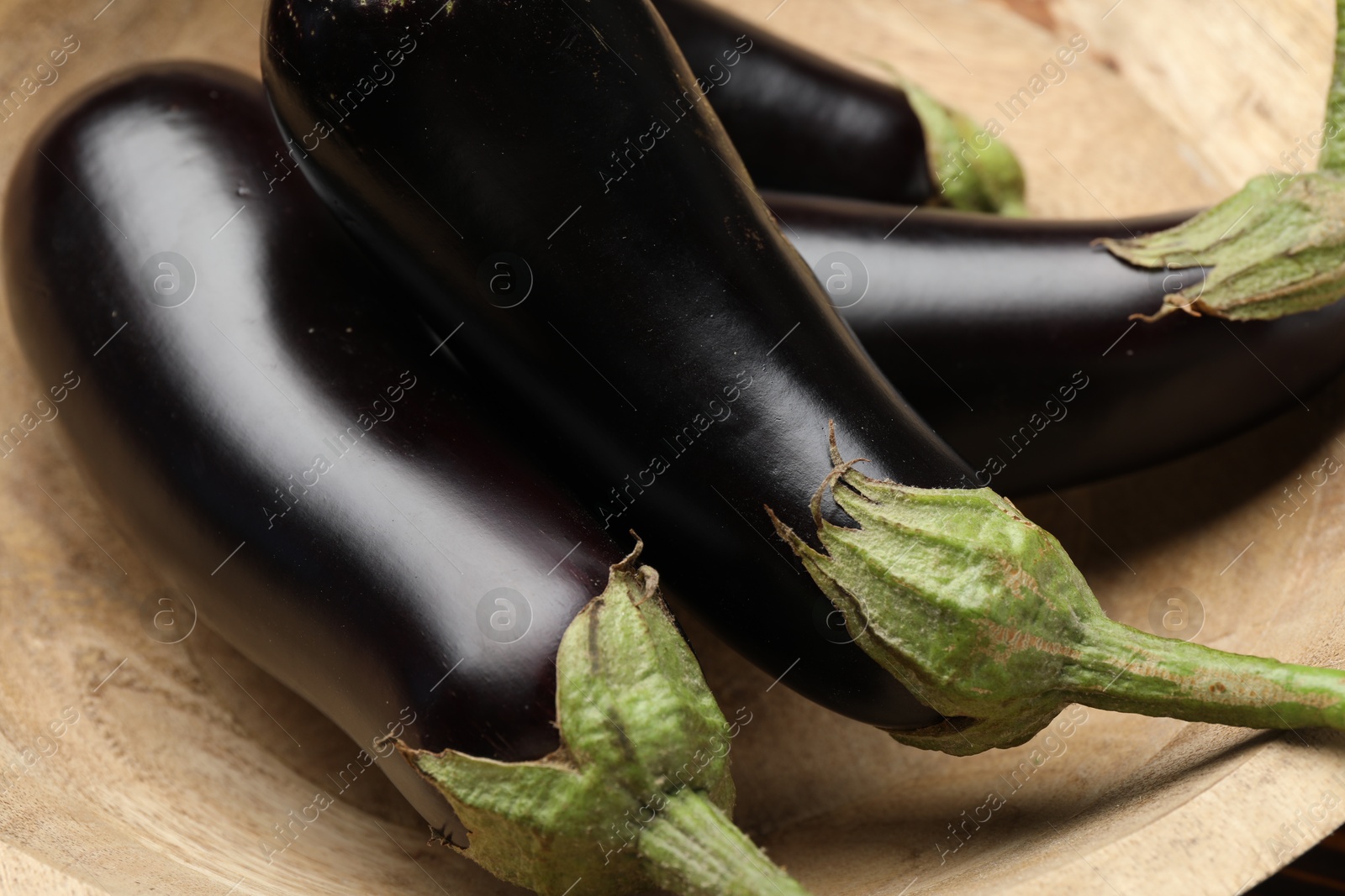 Photo of Whole fresh eggplants in wooden bowl, closeup