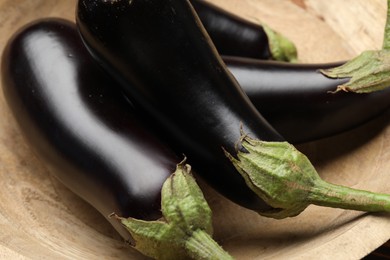 Photo of Whole fresh eggplants in wooden bowl, closeup