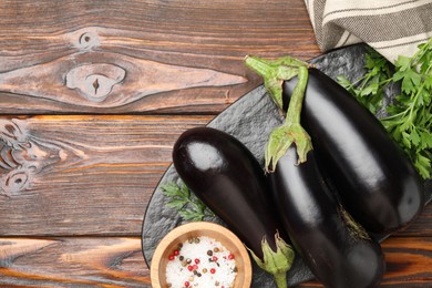 Photo of Fresh eggplants, parsley and spices on wooden table, flat lay. Space for text