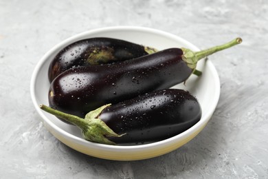 Photo of Fresh wet eggplants in bowl on grey textured table, closeup