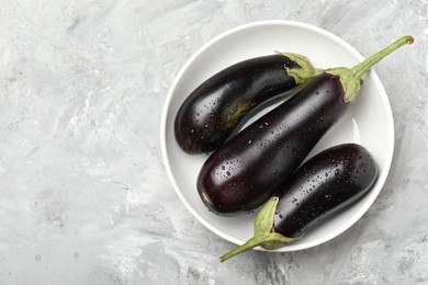 Photo of Fresh wet eggplants in bowl on grey textured table, top view. Space for text
