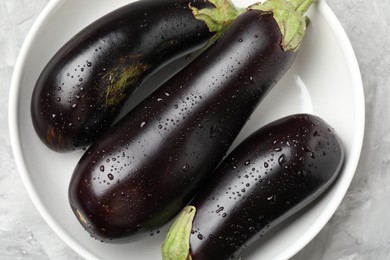 Photo of Fresh wet eggplants in bowl on grey table, top view