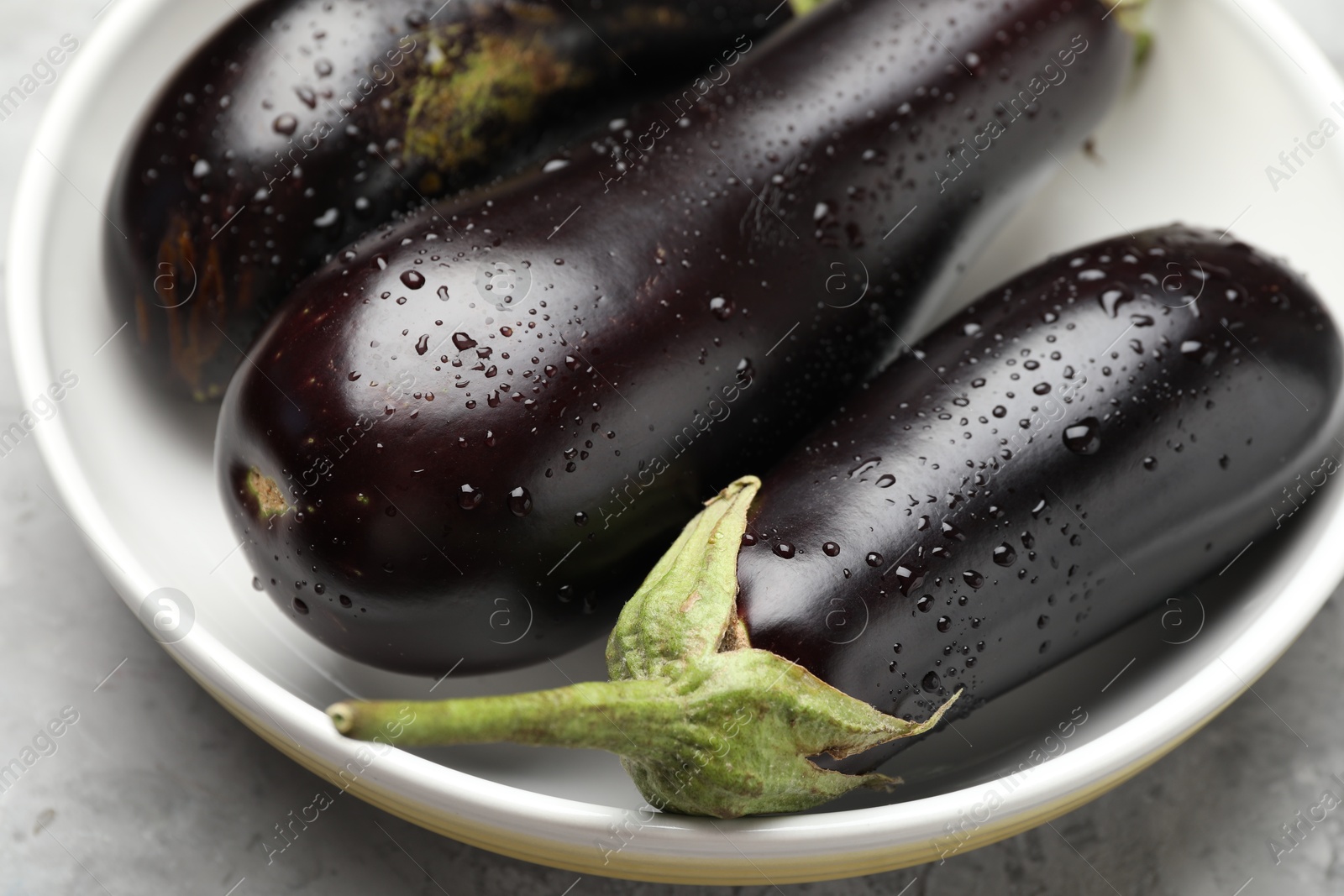 Fresh wet eggplants in bowl on grey textured table, closeup Photo of Fresh wet eggplants in bowl on grey textured table, closeup