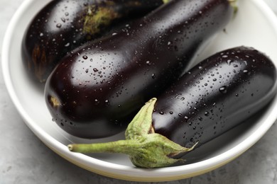 Photo of Fresh wet eggplants in bowl on grey textured table, closeup