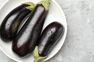 Photo of Fresh wet eggplants in bowl on grey textured table, top view. Space for text