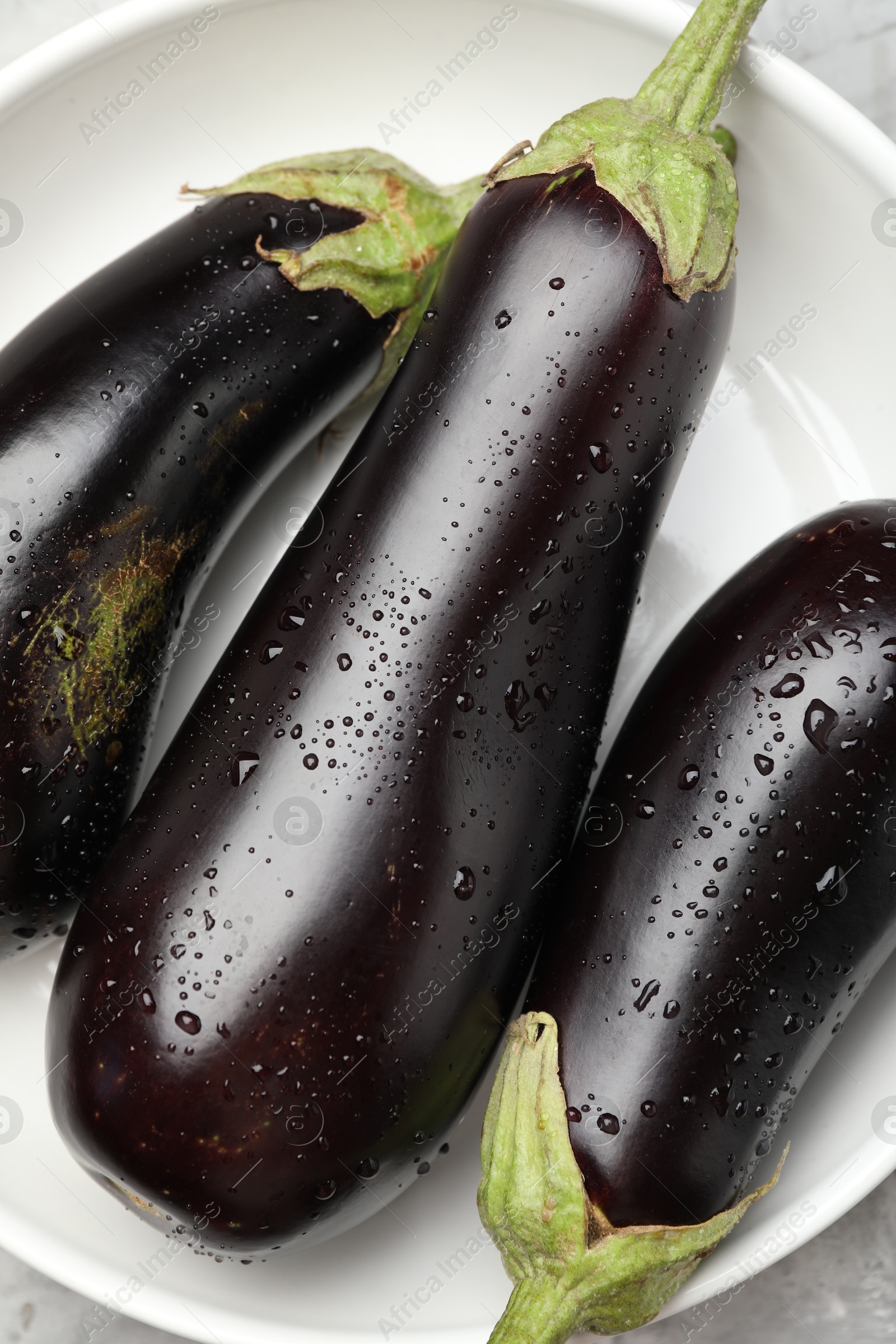 Photo of Fresh wet eggplants in bowl on grey table, top view