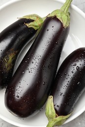 Photo of Fresh wet eggplants in bowl on grey table, top view