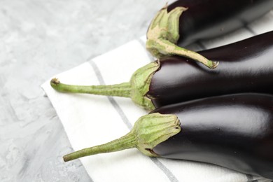 Photo of Fresh eggplants and napkin on grey textured table, closeup