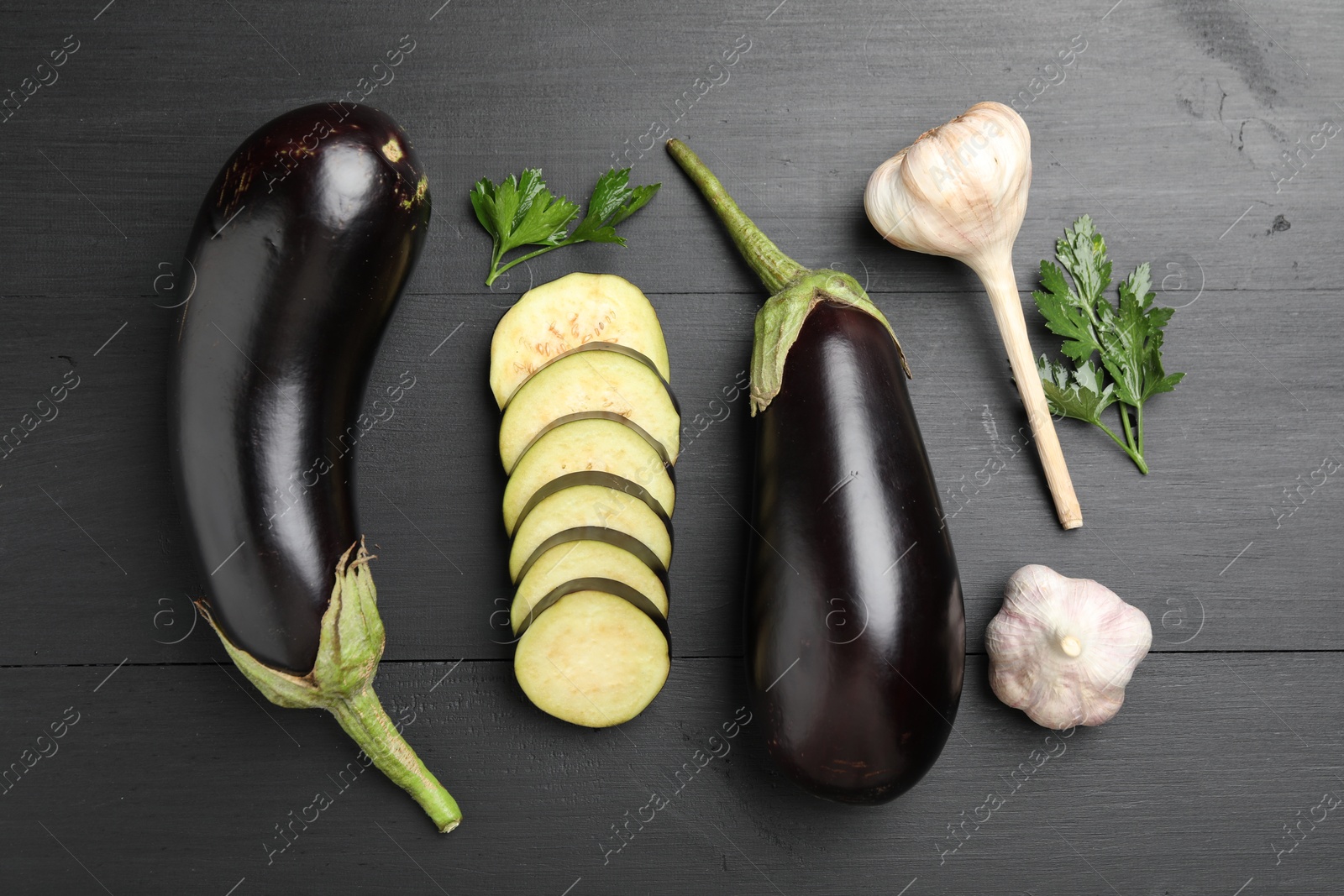 Fresh eggplants, garlic and parsley on black wooden table, flat lay Photo of Fresh eggplants, garlic and parsley on black wooden table, flat lay