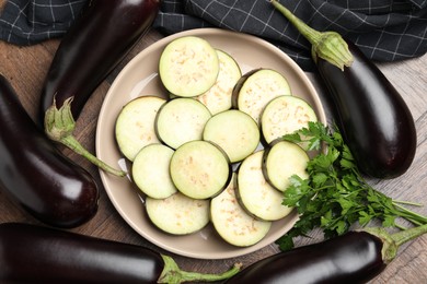 Photo of Slices of fresh eggplants surrounded by whole ones and parsley on wooden table, flat lay