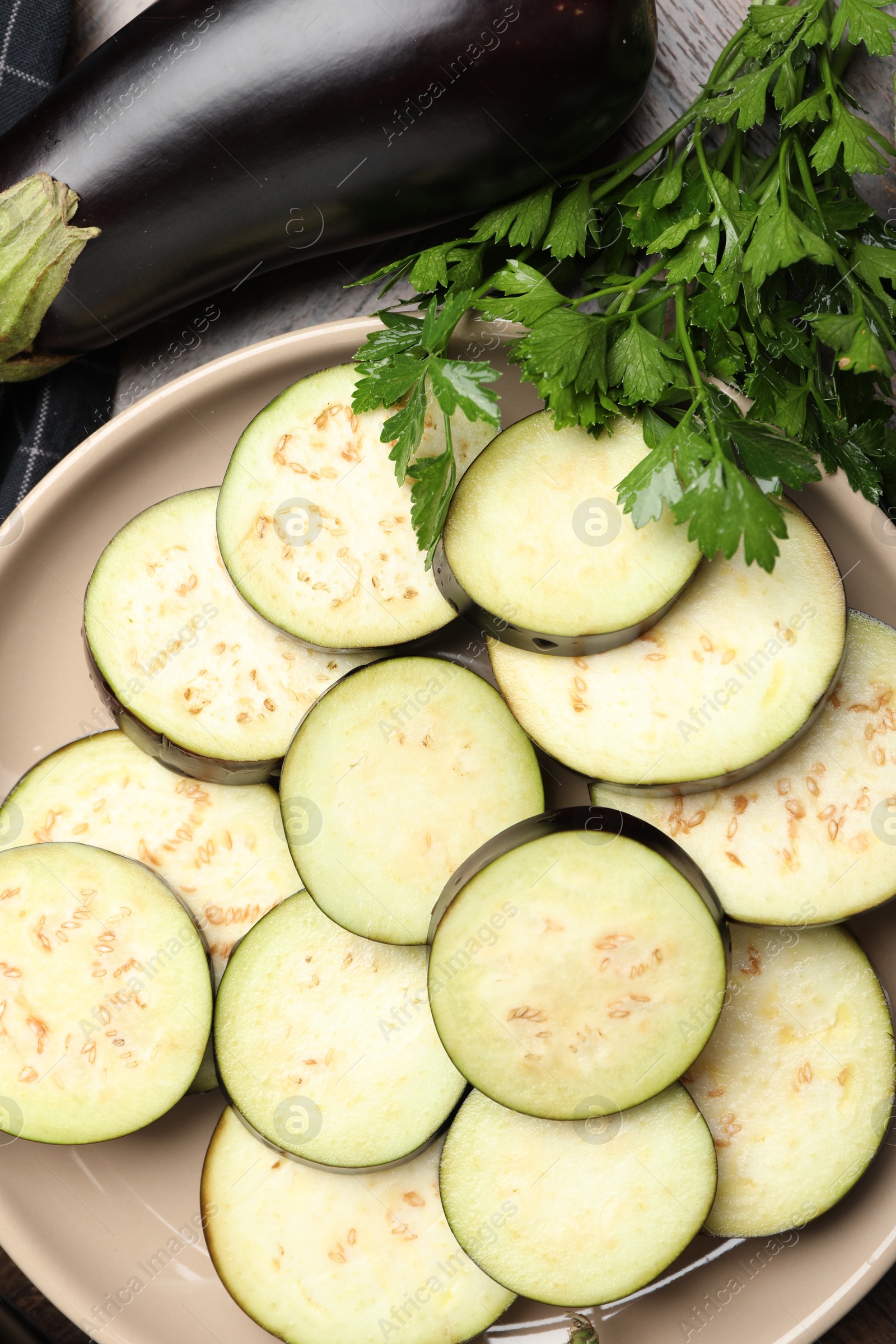 Slices of fresh eggplants, whole one and parsley on wooden table, flat lay Photo of Slices of fresh eggplants, whole one and parsley on wooden table, flat lay