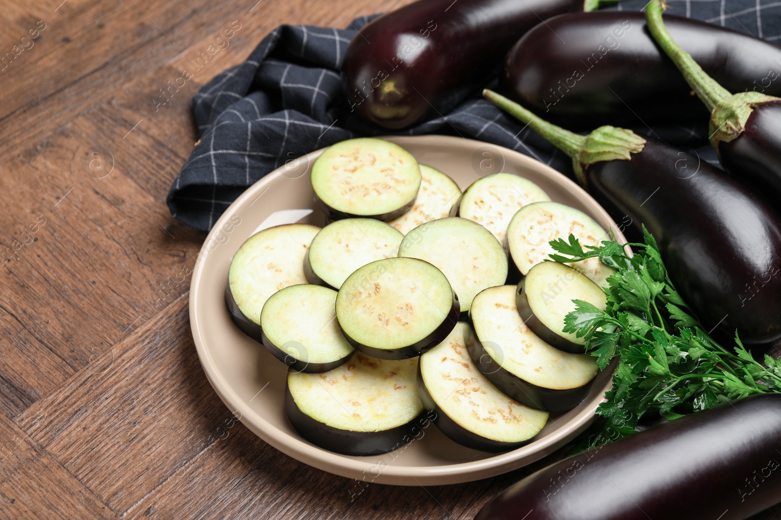 Photo of Slices of fresh eggplants, whole ones and parsley on wooden table, closeup