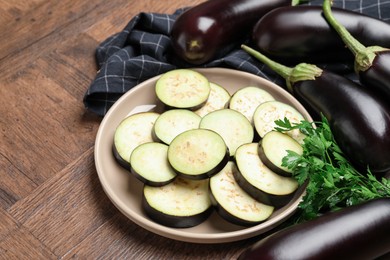 Photo of Slices of fresh eggplants, whole ones and parsley on wooden table, closeup