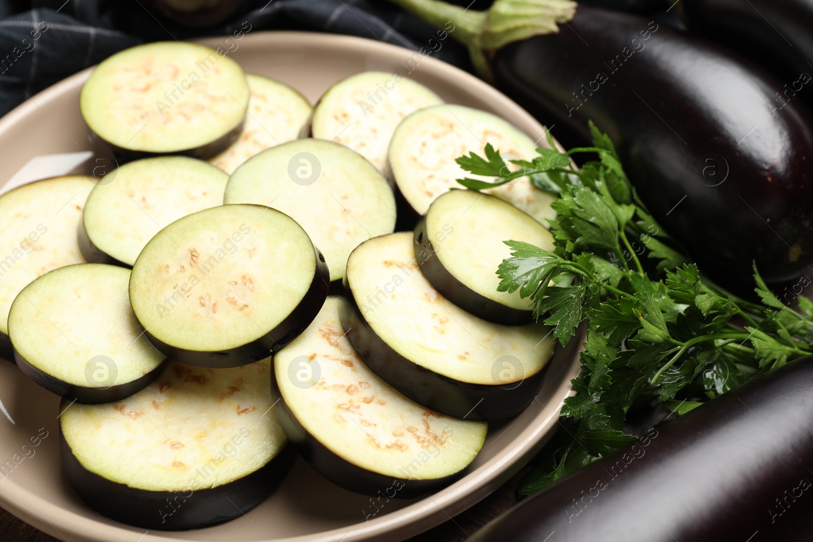 Photo of Slices of fresh eggplants, whole ones and parsley on table, closeup
