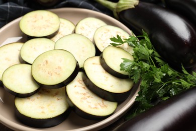 Photo of Slices of fresh eggplants, whole ones and parsley on table, closeup